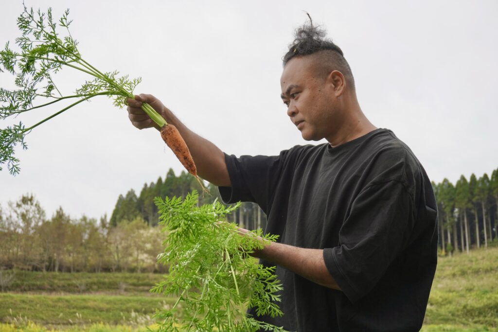 畑で収穫したばかりの人参を見つめる鳥越靖基さん