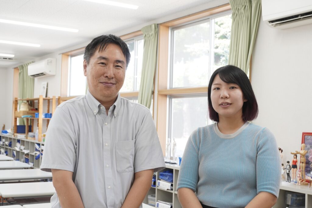 フィギュアも並ぶ教室で写真に収まる教頭と担任