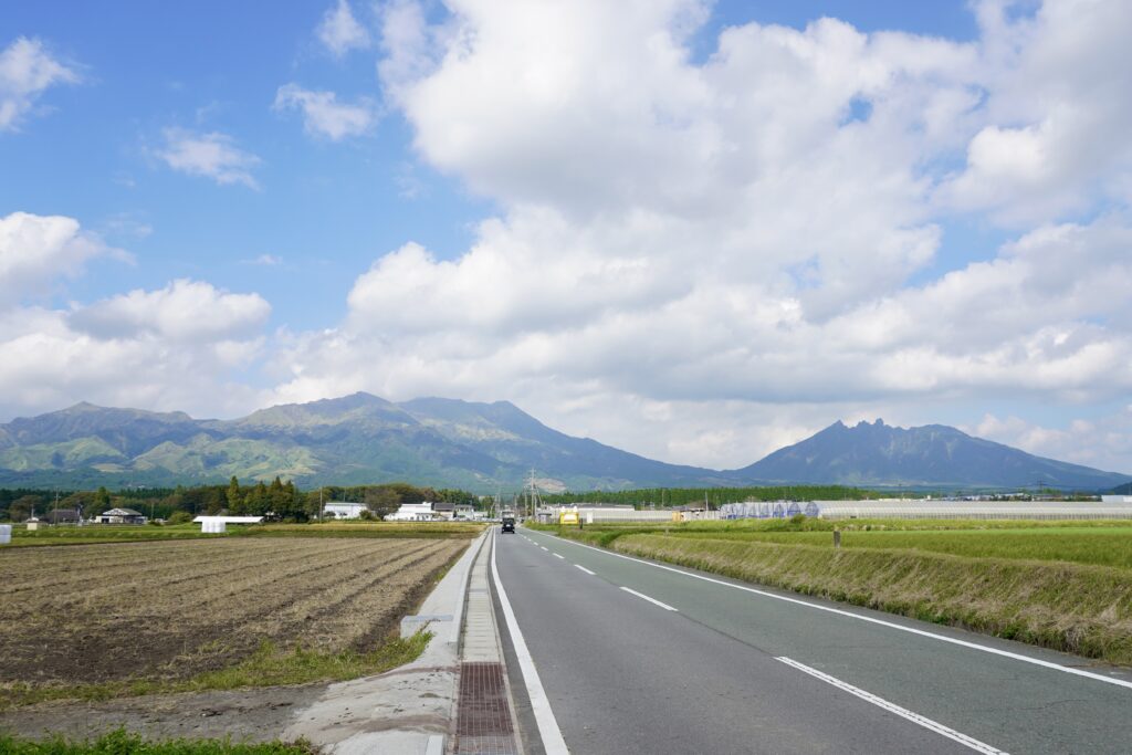 阿蘇五岳の根子岳が見える写真。奥に見える根子岳や山々に向かって、真っすぐの道路が伸びている