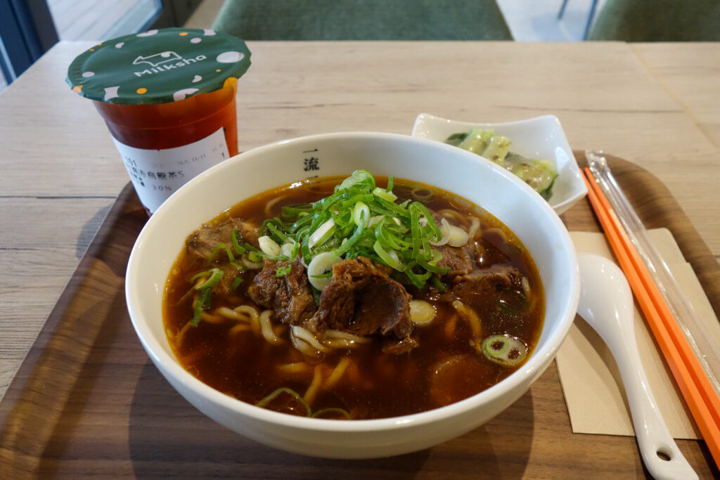 器に盛られた「牛肉麺（ニューローメン）」。黒に近い濃い茶色のスープに、大きな牛肉がゴロゴロと載っている。面は太めで、一番上にはネギがたっぷりかけられている