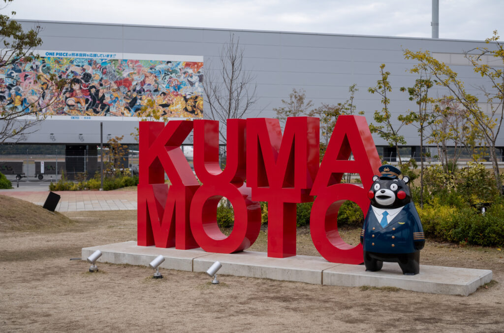 モニュメントの色は赤で、ローマ字でくまもとの形をとっている。その横には飛行機のパイロットの制服と帽子を身に着けたくまモンの人形が置いてある